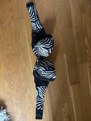 Zebramönstrad push-up bh med spets - Snygg push-up bh med zebramönster i svart och vitt. Kuporna är vadderade och dekorerade med svart spets längs kanterna. Axelbanden är breda och mönstrade, och bh:n har hakknäppning bak. Materialet är en mix av tyg och spets för en cool look.