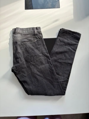 Svarta raka jeans med klassisk look - Säljer ett par svarta jeans med rak passform och klassisk femficksdesign. Jeansen har en knappstängning och är tillverkade i denim med lätt tvättad finish. Perfekta för dig som gillar en enkel och tidlös stil.