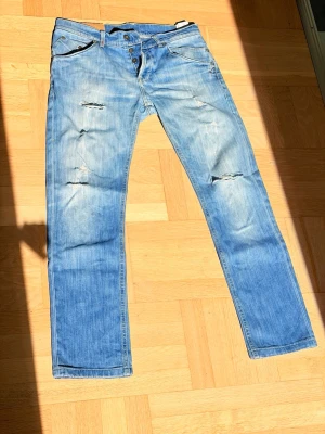 Dondups sammy - Säljer ett par ljusblå dondup jeans med slitningar och hål på framsidan. Jeansen har raka ben, klassisk femficksmodell och knappgylf. Perfekta för en avslappnad och trendig look. Materialet är denim i bomull. Kom gärna med prisförslag eller frågor! 😁Sitter mer som 31-30W