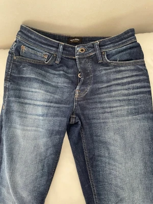 Herr jeans från Jack & Jones  - Snygga blå jeans från Jack & Jones med klassisk femficksmodell och slitna detaljer framtill. Jeansen har normal midja, raka ben och är tillverkade i denim med tydliga tvätteffekter. Perfekta för en avslappnad och trendig stil.