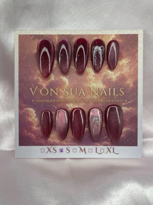 Satin (S);Medium Almond - Handgjorda press-on naglar i vinröd cateye i en medium lång mandelform. Två av naglar har vita rosetter för en unik look. Perfekt för dig som vill sticka ut med snygga detaljer och trendig färg.S: 15 mm, 11,5 mm, 12 mm, 11 mm, 9 mm 