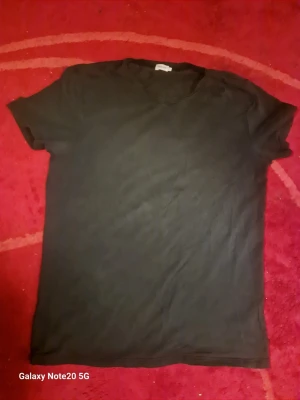 Svart t-shirt från Filippa K - En klassisk svart t-shirt från Filippa K i storlek XL. T-shirten har rund halsringning och korta ärmar, perfekt för en enkel och stilren look. Tillverkad i mjuk bomull som känns skön mot huden.