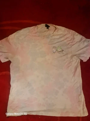 Tie-dye t-shirt med Rick & Morty print - Säljer en ljus tie-dye t-shirt med Rick & Morty-motiv både fram och bak. T-shirten har korta ärmar och rund hals. Trycket visar karaktärerna och texten 'Wubba Lubba Dub Dub'. Perfekt för dig som gillar tecknade serier och vill sticka ut.