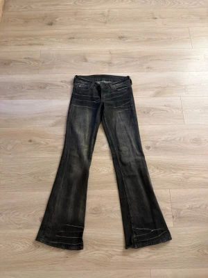 Svarta bootcut jeans med slitningar - Säljer ett par svarta bootcut jeans med snygga slitningar och tvättade detaljer. Jeansen har klassisk femficksmodell och utsvängda ben. Perfekta för dig som gillar en retro och avslappnad stil.