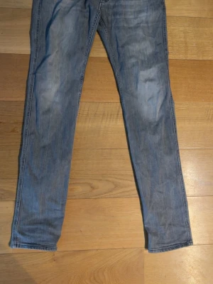 Replay anbass - Säljer ett par gråa slim fit jeans med klassisk femficksdesign och diskreta slitningar framtill. Jeansen har normal midja och raka ben, perfekta till en avslappnad look. Materialet känns mjukt och följsamt, troligen bomull med lite stretch.