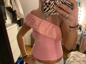 Rosa oneshoulder topp med volang - Säljer en ljusrosa oneshoulder topp med bred volangdetalj över bröstet. Toppen är tight och ärmlös