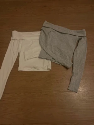 Offshoulder toppar i vitt och grått - Två snygga offshoulder toppar i vitt och ljusgrått. Båda har lång ärm och en bred kant upptill som ger en trendig look. Perfekta att matcha med jeans eller kjol för en cool outfit.