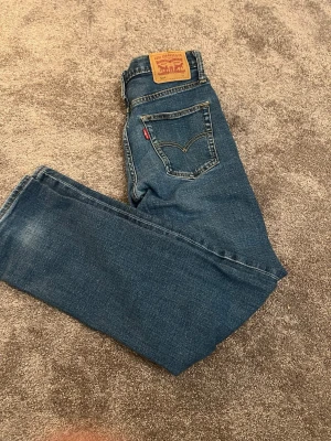 Blå regular jeans från Levi's - Klassiska blå jeans från Levi's med rak passform och fem fickor. Jeansen har den ikoniska läderlappen bak i midjan och röda Levi's-taggen på bakfickan. Tillverkade i slitstark denim med snygga detaljer och kontrastsömmar.