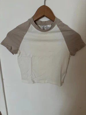 Beige och vit croppad t-shirt - Säljer en croppad t-shirt med beige ärmar och vit kropp. T-shirten har rund halsringning och korta ärmar🤍