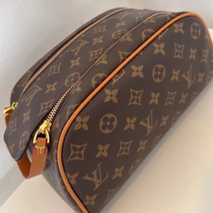 Brun stor och praktisk necessär i modern modell. Mönster i populärt monogram - Snygg brun necessär i klassiskt brunt monogrammönster med snygga detaljer. Necessären har guldfärgade dragkedjor och läderdetaljer i kanterna. Perfekt för att organisera dina hygienartiklar, smink och småsaker när du är på språng eller snygg att ha i badrummet hemma. 