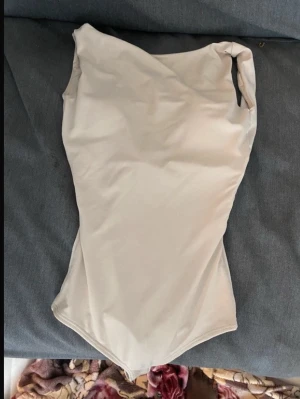 Beige enkel baddräkt - Stilren beige baddräkt med klassisk skärning och breda axelband. Tillverkad i ett stretchigt material som ger en bekväm passform. Perfekt för strand eller pool och lätt att matcha med andra plagg.