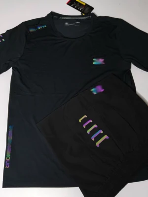 Svart träningsset med färgglada detaljer - Säljer ett svart träningsset med t-shirt och shorts. Setet har färgglada, reflekterande detaljer på både tröjan och shortsen. Materialet känns lätt och andas, perfekt för träning eller sportaktiviteter.