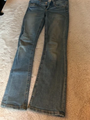 Ljusblå bootcut jeans - Säljer ett par ljusblå jeans med bootcut passform och klassisk femficksdesign. Jeansen har en lätt tvättad look och raka ben som slutar i en något utsvängd kant. Perfekta för en avslappnad och trendig stil.