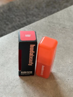 Huda Beauty Blush Filter Sunset Lychee - Flytande rouge från Huda Beauty i nyansen Sunset Lychee. Kommer i en kompakt, fyrkantig orange förpackning med matchande kartong. Ger en fräsch, varm ton till kinderna och är enkel att applicera tack vare sin smidiga formula.