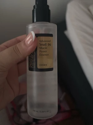 COSRX Snail 96 Mucin Power Essence - Populär toner från COSRX med snigelsekret, Advanced Snail 96 Mucin Power Essence. Kommer i en genomskinlig plastflaska med svart pump och guldig etikett. Innehåller 100 ml och har en lätt, klar formula som återfuktar och stärker huden.