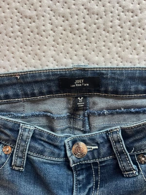 Blå low rise flare jeans Joey - Snygga blå jeans med låg midja och flare-modell från Joey. Jeansen har dekorativa sömmar och ficklock bak med knappdetalj. Klassisk femficksdesign och slitstark denim med ljus tvätt. Perfekta för en trendig och avslappnad stil.