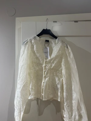 Vit blus med knappar från TINSEL - Stilren vit blus från ginatricot. Helt ny och oanvänd med lapp kvar.  Blusen har v-ringning och dekorativa knappar framtill. Den har dessutom  långa, puffiga ärmar. Superfin men fel storlek tyvärr 🌸 