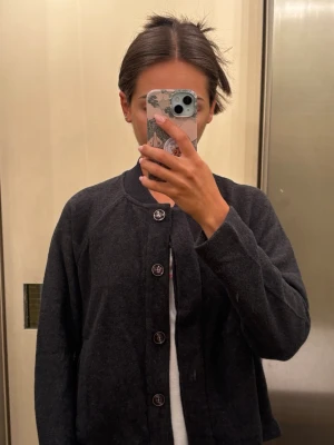 Mörkgrå knappad cardigan - Mysig mörkgrå cardigan med rund halsringning och knappar framtill. Tillverkad i en mjuk blandning av bomull, polyester, viskos och akryl. Perfekt att slänga över en t-shirt för en chill look.