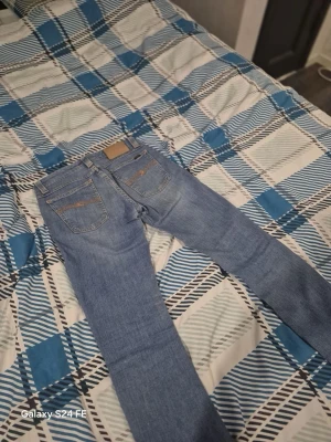 Nudie jeans  - Säljer ett par nudie jeans i klassisk modell med raka ben och fem fickor. Jeansen har snygga slitningar och kontrastsömmar på bakfickorna. Tillverkade i denim med bälteshällor och knappgylf. Perfekta för en avslappnad stil.