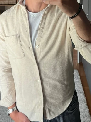 Samsøe Samsøe överskjorta i beige - stl M - Samsøe Samsøe överskjorta i beige, storlek M. 100% ekologisk bomull, borstad flanell som är mjuk och tjockare än en vanlig skjorta. Bröstficka och rundad nederkant. Bra som lager över t-shirt när det är svalt. Personen på bilden är 189cm, väger 78kg.  Använd men i mycket fint skick, inga hål eller fläckar.  Rök- och djurfritt hem. Skriv gärna om du vill ha fler bilder eller undrar något!