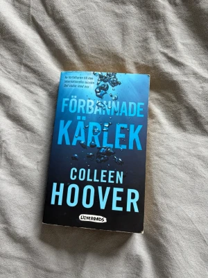 Förbannade kärlek av Colleen Hoover - En fängslande roman av Colleen Hoover med blått och svart omslag. Boken är på svenska och handlar om Tate och Miles, och deras komplicerade relation. Perfekt för dig som gillar romantik och drama. Pocketutgåva från Lovereads.