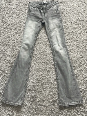 Ljusgrå bootcut jeans - Säljer ett par ljusgrå bootcut jeans med klassisk femficksdesign. Jeansen har utsvängda ben och detaljerade bakfickor. Perfekta för dig som gillar en avslappnad men trendig stil. Storlek 158. Inte använd. 