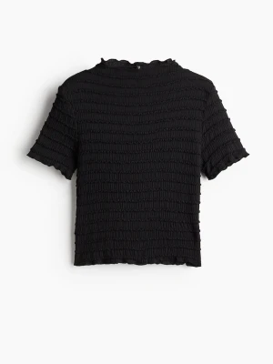 Svart ribbad topp med kort ärm - Säljer en svart ribbad topp med korta ärmar och stretchig, smockad struktur. Toppen har en något croppad passform och vågig kant vid ärmslut och nederkant. Perfekt att styla med jeans eller kjol för en trendig look. Bara använd fåtal gånger
