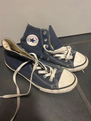 Blå Converse All Star high tops - Klassiska blå Converse All Star high tops med vit tå och vita snören. Storlek 35, bra skick, men har lite fläckar på sulan på undersidan (se bilder)