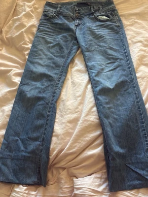 Blå bootcut jeans med knappar - Säljer ett par klassiska blå bootcut jeans i denim med snygga kontrastsömmar och knappgylf. Jeansen har fem fickor och en ljus tvätt som ger en avslappnad look. Perfekta för dig som gillar retrostil och vill ha ett par jeans med lite vidare ben, jag köpte de av en tjej på vinted men de va för stora tyvärr men jag har använt en speciell tejp som gör att de blir kortare så dom är kortare i längden så hör av er för mått !!💕 de står storlek 33 så antar w33