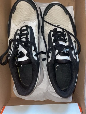 Nike svartvita sneakers - Nike sneakers i svart och vitt med mesh-ovandel och svarta snören. Skorna har en sportig look med låg profil och bekväm sula, perfekta för dig som gillar streetwear och sportig stil.