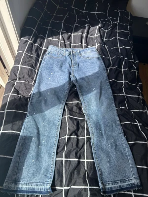 Blå flared jeans med splatterdetaljer – Storlek M  - Helt nya blå jeans med snygga vita splatterdetaljer och råa detaljer längst ner. Endast testade och aldrig använda ute. Storlek M. Snygg och modern passform som passar perfekt till både sneakers och streetwear.  📏 Storlek: M W32 L30 ✨ Skick: Helt nya – endast testade 🎨 Färg: Ljusblå/denim 📦 Skickas snabbt och välpackat! 