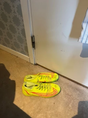 Gula Nike Mercurial fotbollsskor - Säljer ett par grymma Nike Mercurial fotbollsskor i neon-gult med röda detaljer och snörning. Skorna har låg profil och är tillverkade i syntetmaterial för bästa grepp och känsla på planen. Perfekta för dig som vill sticka ut på matchen!