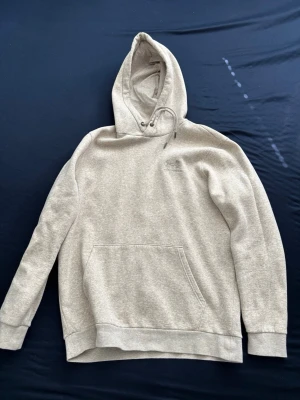 Beige Under Armor hoodie  - Säljer en stilren beige hoodie med klassisk magficka och justerbar huva med dragsko. Hoodien har ribbade muddar vid ärmslut och nederkant. Perfekt för en avslappnad och bekväm look.
