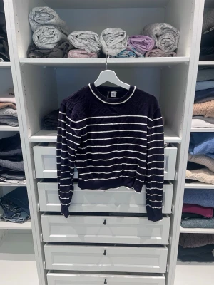 Mörkblå stickad tröja från H&M - Mörkblå stickad tröja från H&M med vita horisontella ränder. Tröjan har rund halsringning och ribbade muddar vid ärmslut och nederkant. Perfekt för lager på lager och enkel att matcha med jeans eller kjol.
