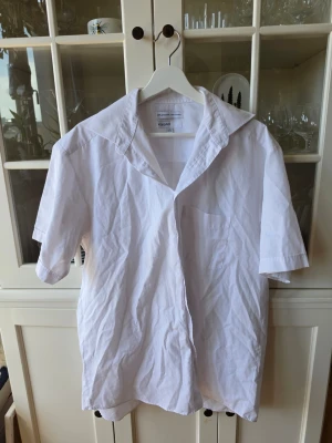 Vit kortärmad skjorta från KappAhl - Klassisk vit skjorta från KappAhl i storlek L. Skjortan har korta ärmar, öppen krage och en bröstficka. Tillverkad i en mix av polyester och bomull vilket gör den lätt och bekväm. Perfekt till sommaren och enkel att matcha.