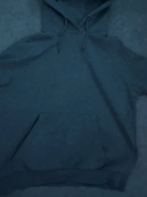 grå ryvl hoodie me snören  - En enkel och stilren grå hoodie med klassisk magficka och justerbar huva med dragsko. Tillverkad i mjukt sweatshirtmaterial som är skönt mot huden. Perfekt för chill dagar eller när du vill ha en avslappnad look.