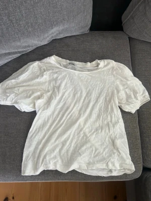 Vit T-shirt med volang ärm - Enkel, söt topp med volang  ärm. Perfekt för varma dagar då materialet är tunt och luftigt. 