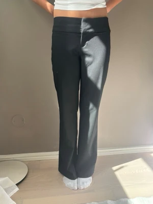 Svarta kostymbyxor med normal midja - Snygga svarta kostymbyxor med normal midja och raka ben. Byxorna har en minimalistisk design utan synliga fickor eller detaljer och är tillverkade i ett slätt tyg som ger en stilren look. Perfekta för dig som gillar en clean och modern stil. HELT OANVÄNDA