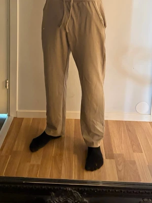 Beige mjukisbyxor med dragsko | Lager 157 - Säljer ett par beige mjukisbyxor med raka ben och dragsko i midjan. Byxorna har sidofickor och är gjorda i ett mjukt, bekvämt material som passar perfekt för chill dagar. Enkel och stilren design som funkar till det mesta.