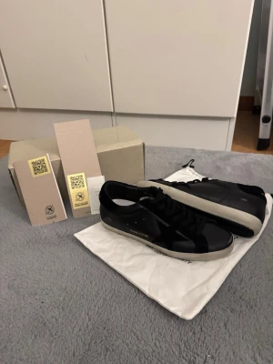 Svarta sneakers från Golden Goose - Stilrena svarta sneakers från Golden Goose med vit sula och diskret logga på sidan. Skorna har klassisk låg profil, svarta skosnören och är tillverkade i läder med detaljer i textil. Perfekta för en trendig och avslappnad look.