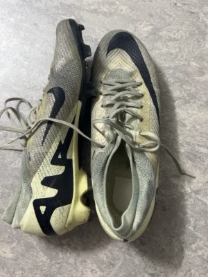 Nike Mercurial fotbollsskor gul/svart - Säljer ett par Nike Mercurial fotbollsskor i ljusgul och svart. Skorna har snörning, klassisk låg profil och tydliga dobbar för bra grepp på planen. Swoosh-logga på sidan och AIR-detalj i svart. Perfekta för dig som vill ha snabba fötter på fotbollsplanen.