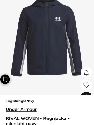 Under Armour mörkblå regnjacka - Snygg regnjacka från Under Armour i färgen midnight navy med vita detaljer längs sidorna. Jackan har huva, dragkedja framtill och logga på bröstet. Tillverkad i ett lätt, vattenavvisande material som passar perfekt för blöta dagar.
