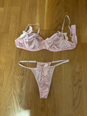 Underkläder strl M/75C - 50kr/set. Säljer två olika set med bodys och stringtrosor. Ett set är ljusrosa med stora rosetter och satinmaterial, och det andra är rött med dekorativa kedjor, hjärtformad detalj och rosetter. Båda seten har smala axelband och en sexig design.