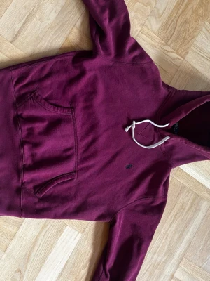 Vinröd hoodie från Polo Ralph Lauren - Säljer en vinröd hoodie från Polo Ralph Lauren med klassisk känguruficka och vit dragsko i huvan. Hoodien har det lilla broderade Polo-logot på bröstet och är gjord i mjukt bomullsmaterial. Perfekt för en chill och stilren look.