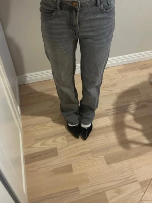 Grå raka jeans med hög midja - Säljer ett par grå jeans med rak passform och hög midja. Jeansen har klassiska fem fickor och stängs med knapp och dragkedja. Materialet är denim i en tvättad grå nyans som ger en avslappnad look. Perfekta till sneakers eller boots. Barnstorlek men passar mig som är xs/s även långa på mig som 158!