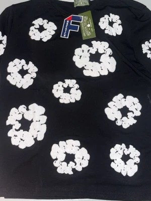 Svart t-shirt och shorts från Denim Tears - Svart t-shirt och shorts från Denim Tears med vita blommönster över hela tröjanoch shortsen. Perfekt för dig som vill sticka ut med en unik och trendig look.
