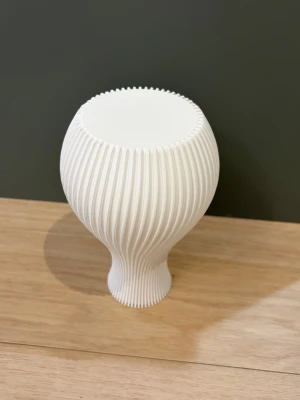 Vit ribbad vas i modern design - Säljer en stilren vit vas med ribbad struktur och rundad form. Vasen är tillverkad i plast och har en smal hals som öppnar upp till en bredare kropp. Perfekt som dekoration eller för blommor i hemmet.