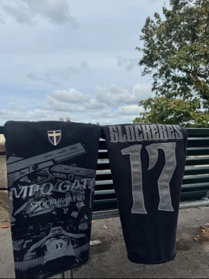 Svart oversized t-shirt med tryck - Cool svart oversized t-shirt med stort grafiskt tryck framtill och texten 'GLOCKERES’  17' på ryggen. T-shirten har korta ärmar och en avslappnad passform. Perfekt för dig som gillar streetwear och sportiga vibbar.