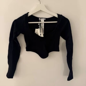 Svart croppad långärmad topp - Trendig svart croppad topp med lång ärm och djup v-ringning. Tillverkad i ett stretchigt material som sitter snyggt på kroppen. Perfekt att styla med höga jeans eller kjol för en cool look.