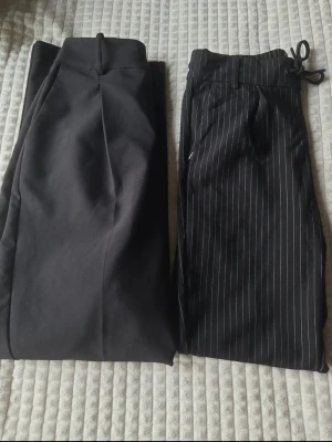 Säljer ett snyggt byxpaket med två par stilrena byxor! 👖✨ - Paketet innehåller: 🖤 Ett par svarta högmidjade kostymbyxor från gina tricot – perfekta både till vardags och mer uppklädda outfits. 🤍 Ett par randiga finbyxor från only som ger en snygg och stilren look. Fuskfickor på båda. Byxorna är i fint använt skick utan hål eller andra större fel. Det finns mindre noppor på vissa ställen från användning, men inget som stör passform eller helhetsintryck. Perfekt för dig som vill ha flera snygga byxor till hösten! 🍂 skriv vid frågor